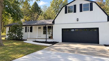 Une maison à deux étages avec un garage, une véranda et un jardin aménagé à l’avant.