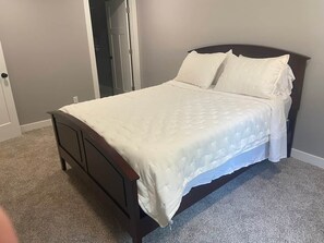 A bedroom with a bed, a door, and a carpeted floor. - At Home on Oak Street (Lynnville)