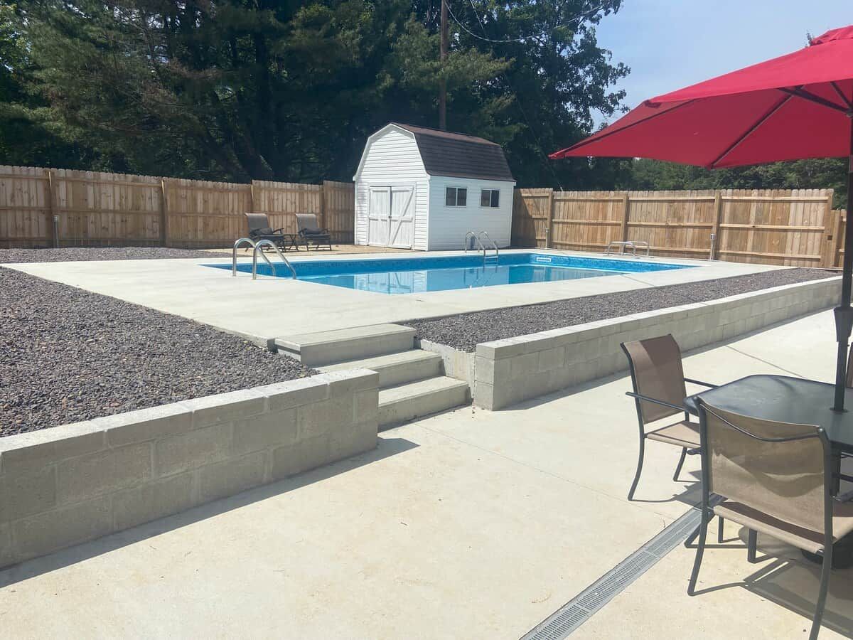 A backyard with a swimming pool, a small shed, and a patio area with a table and chairs.