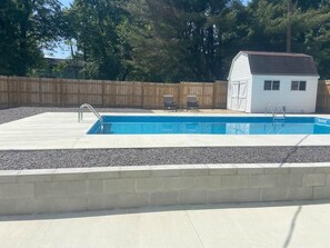 A rectangular swimming pool with a concrete deck, two lounge chairs, and a small shed in the background. - At Home on Oak Street (Lynnville)