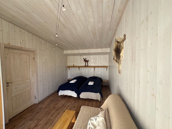 A room with two beds, a wooden bench, a mounted animal head, and a door.