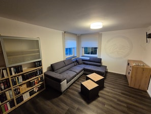 Ein modernes Wohnzimmer mit einem Ecksofa, einem Bücherregal und einer kleinen Holzkabine.