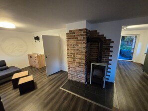 Ein Zimmer mit Kamin, einer Couch, einem Holzkasten und einer Tür zu einem weiteren Raum.