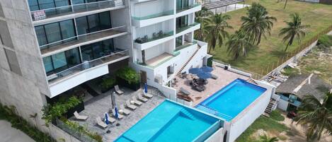 A multi-story hotel with a rooftop pool, outdoor seating, and a view of the surrounding landscape.