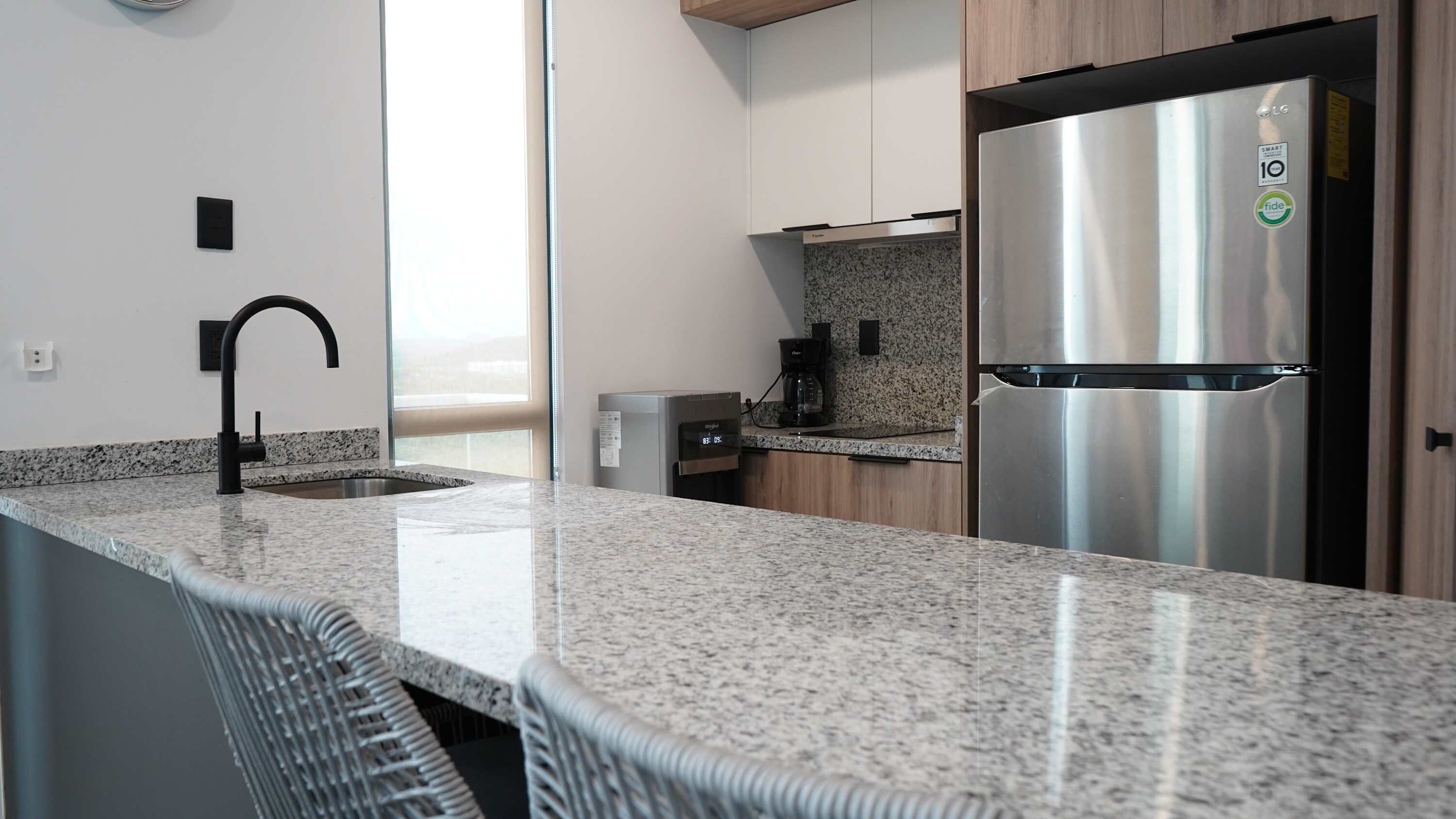 A modern kitchen with granite countertops, a stainless steel refrigerator, and a built-in dishwasher.