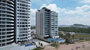 A high-rise hotel with multiple balconies, a rooftop pool, and a view of a beach and distant landscape. - Torre W Beachfront Condo: Ocean View & Pools (Mazatlán)