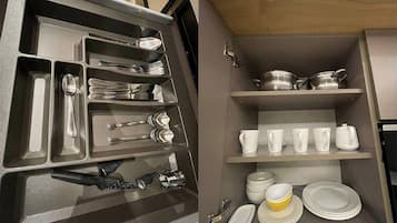 A compact kitchen with built-in storage for utensils and cookware, and a shelf with dishes and cups.