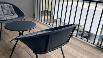 Un balcon avec une chaise et une petite table, une balustrade et une vue sur la rue.