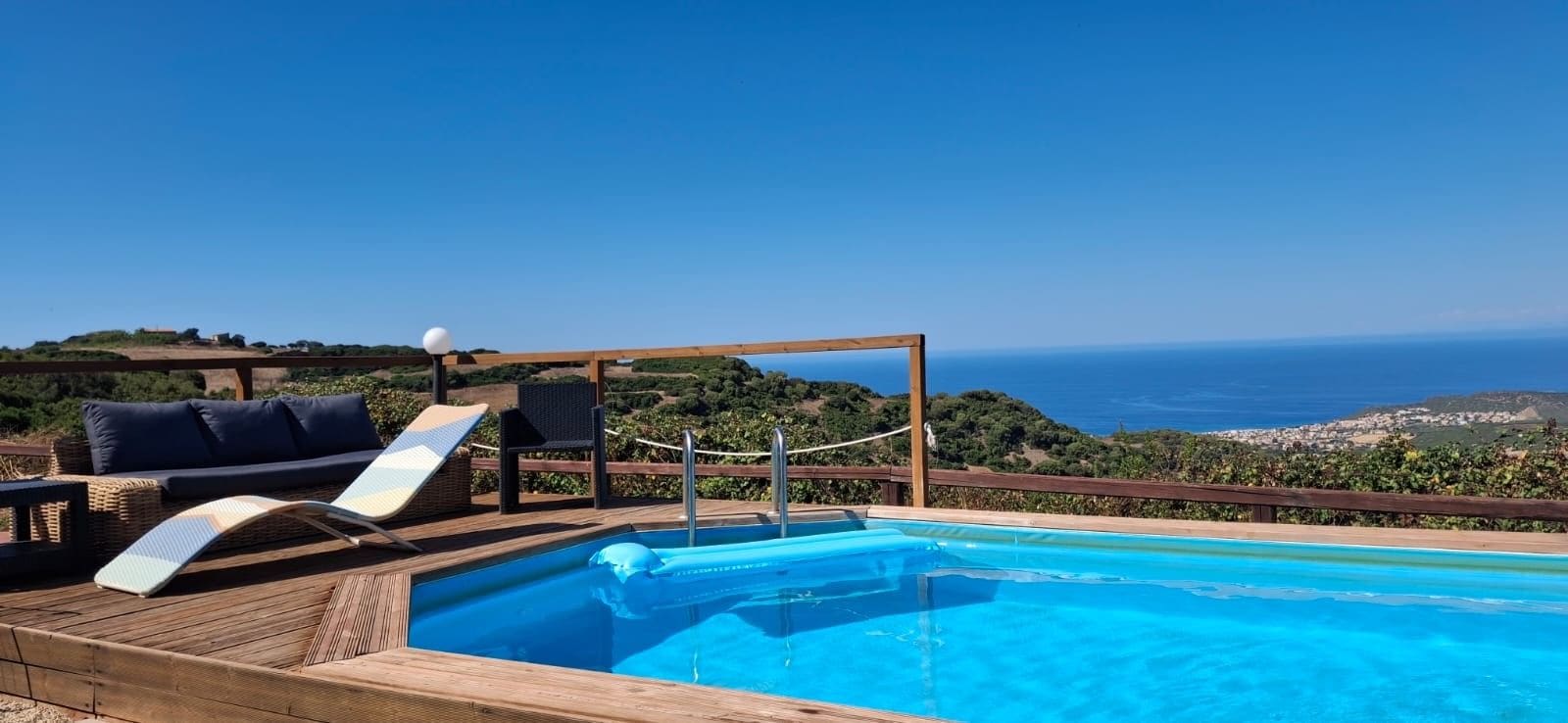 A pool area with a wooden deck, lounge chairs, and a view of the ocean.