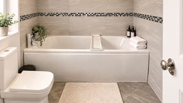 A bathroom with a white bathtub, a toilet, and a small rug.