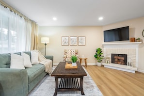 A living room with a green sofa, a wooden coffee table, a fireplace, and a TV mounted above it. - Gorgeous 3-bedroom townhome with AC in lovely center of Bellevue (Bellevue)