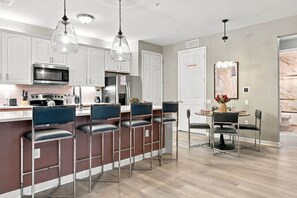 A modern kitchen with stainless steel appliances, a bar area with bar stools, and a dining table with chairs. - Luxury 3BR, Newly Renovated, Lake View, Vista Cay (Orlando)