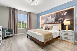 Une chambre moderne avec un grand lit, des lampes de chevet, un fauteuil et une vue sur la verdure par la fenêtre.