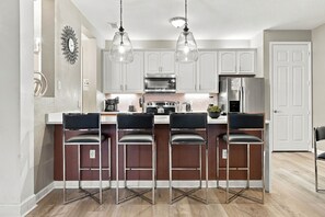A modern kitchen with stainless steel appliances, a central island with bar stools, and pendant lighting. - Luxury 3BR, Newly Renovated, Lake View, Vista Cay (Orlando)
