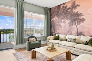 A living room with a view of a body of water, a sofa, a chair, and a coffee table. - Designer Luxury 3BR, Stunning Lake View, Vista Cay (Orlando)