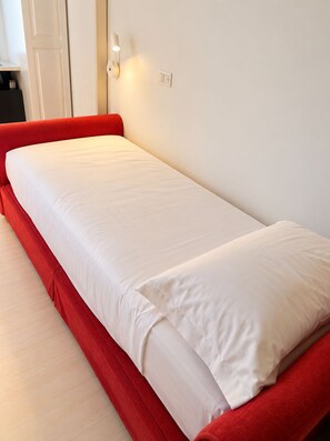 A single bed with a red frame and white bedding in a room with white walls and a wooden floor. - Paris at the Colosseum: The style you've been looking for, in an unforgettable apartment (Roma)