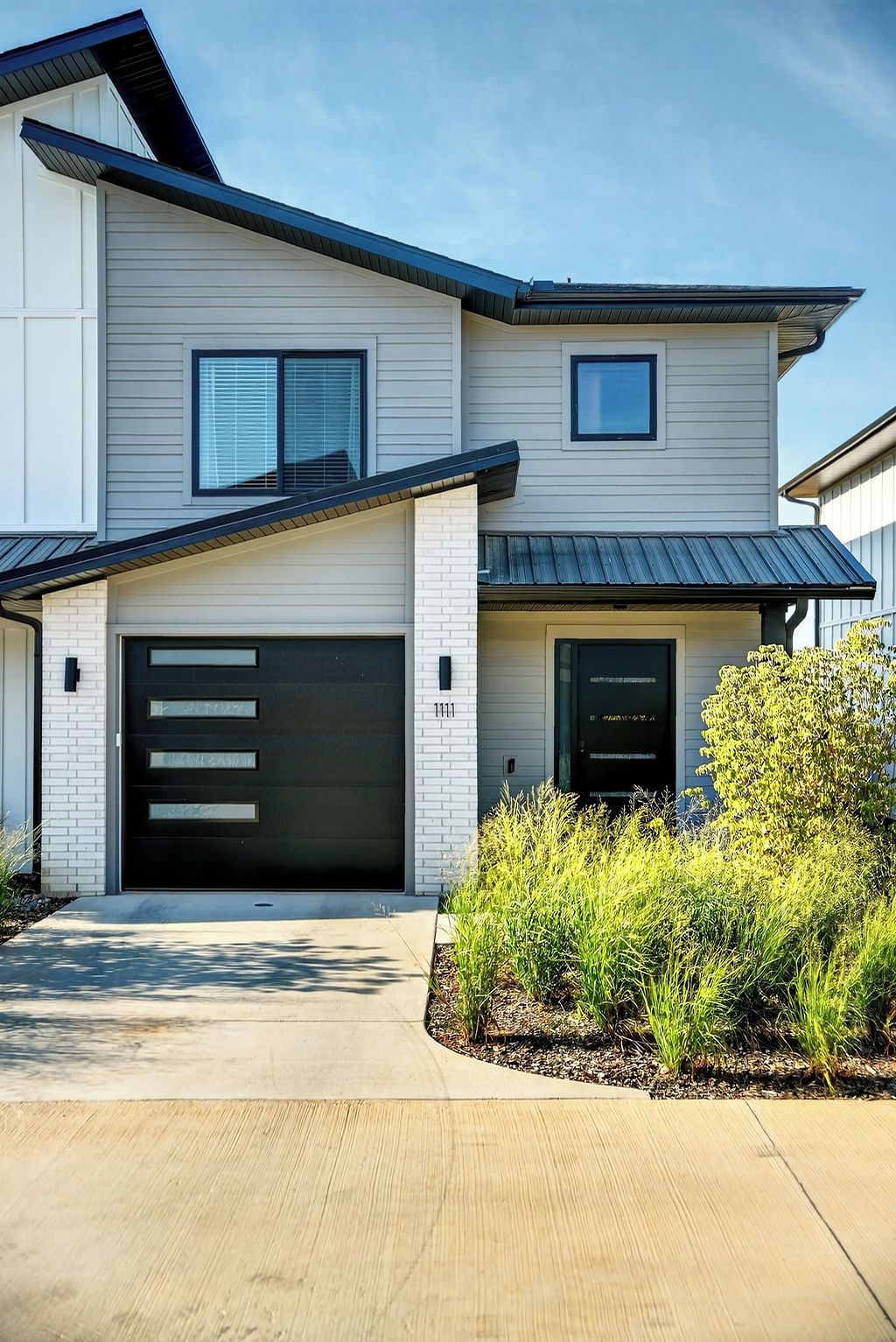 A modern two-story house with a garage, a small front porch, and a well-maintained garden.