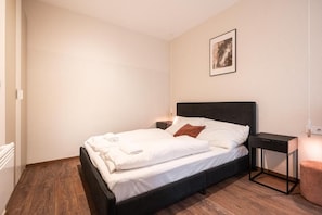 A neatly made bed with white linens and a single brown pillow, a small bedside table with a lamp, and a framed picture on the wall. - Kazinczy 11 - Boutique Apartment by BQA  (Budapest)