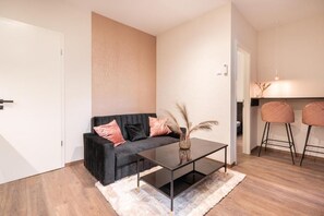 A modern living room with a black sofa, a coffee table, and two bar stools. - Kazinczy 11 - Boutique Apartment by BQA  (Budapest)