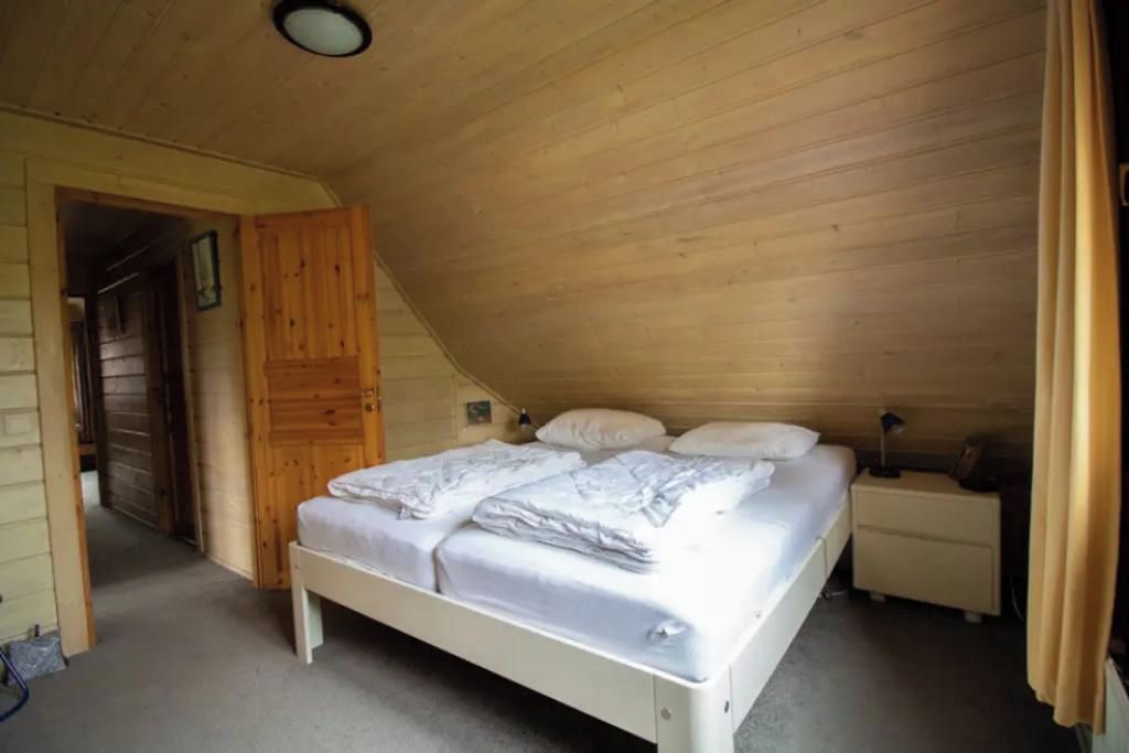 A single-bed room with a sloped ceiling, wooden walls, a bedside table, and a nightstand.