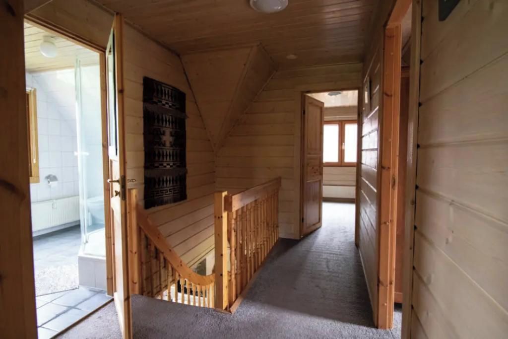 A wooden interior with a staircase leading to a lower level, a door to the left, and a window at the end of the corridor.