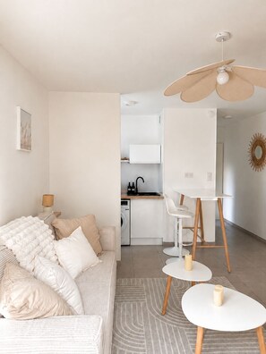 Ein modernes Wohnzimmer mit einer Couch, einem Essbereich mit Tisch und Stühlen, einer Küche mit weißem Schrank und einem Deckenventilator.