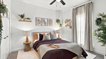 A bedroom with a bed, bedside tables, a ceiling fan, wall art, and a window with curtains.