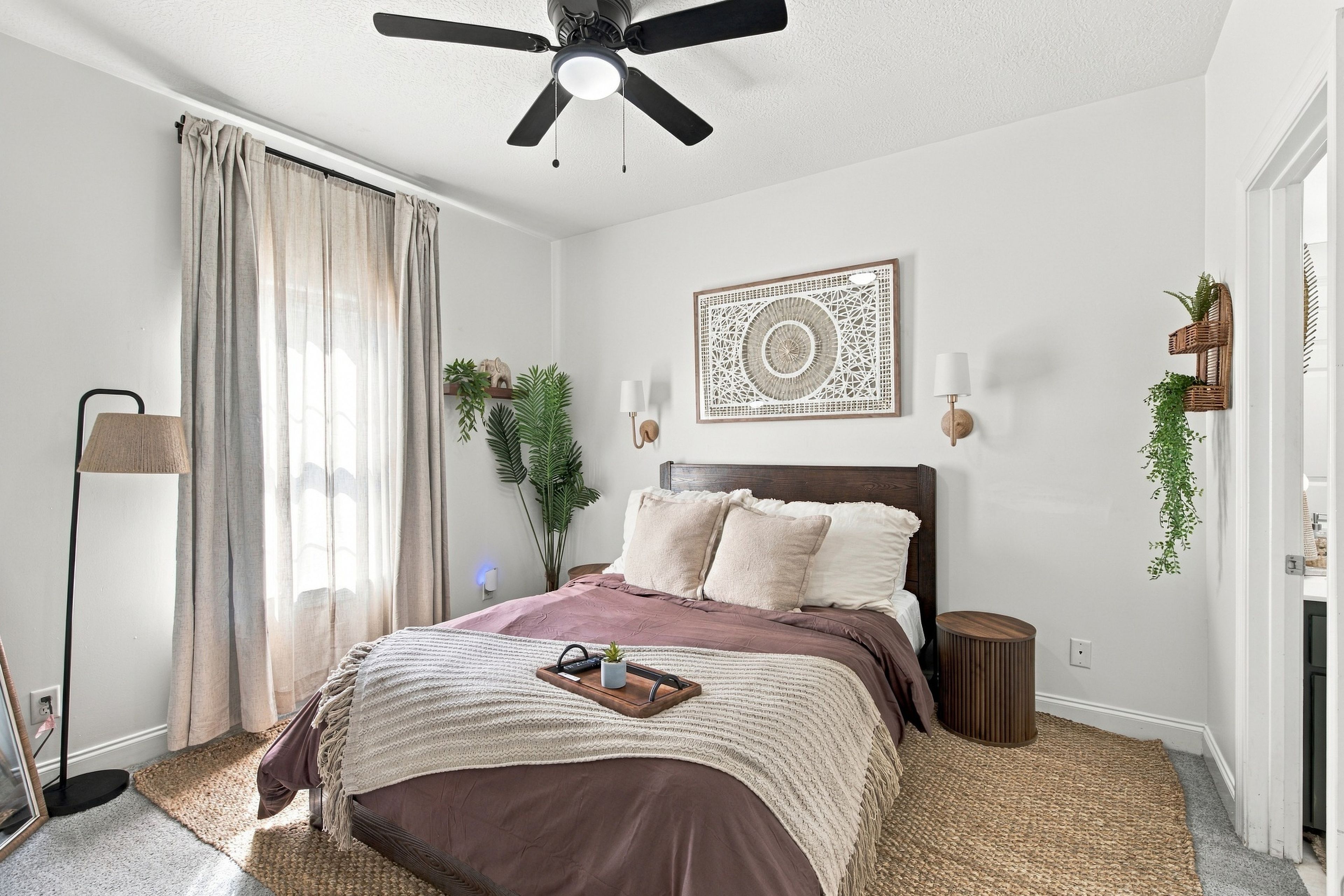 A bedroom with a bed, a ceiling fan, a wall-mounted light, and a decorative wall piece.