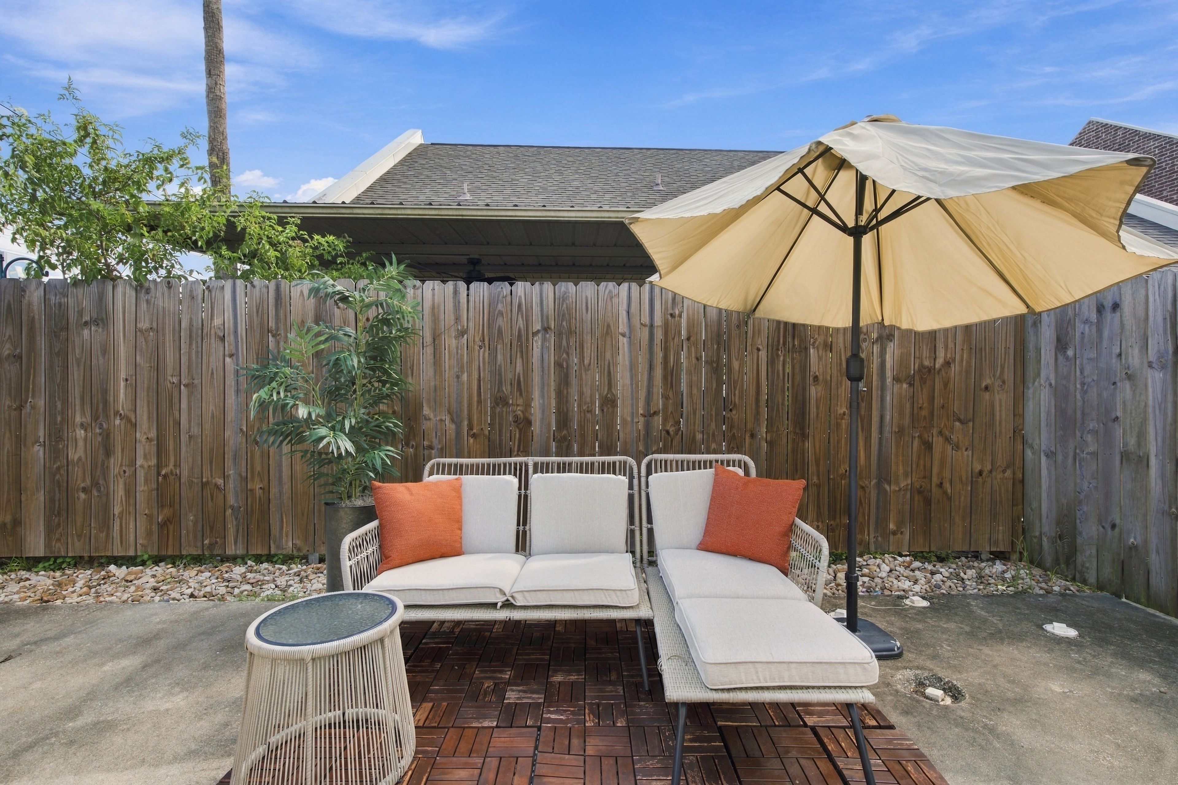 A patio with a white outdoor sofa, a round table, and a large umbrella.