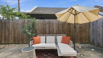 A patio with a white outdoor sofa, a round table, and a large umbrella.