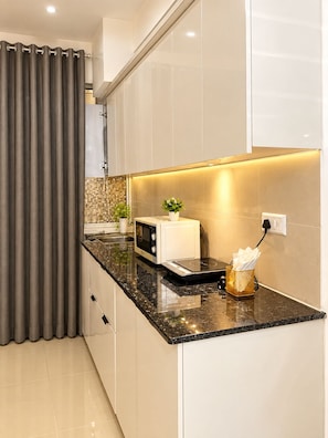 Una cocina moderna con encimera negra, armarios blancos, un microondas y una pequeña planta.