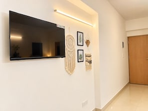 Un pasillo moderno con un televisor de pantalla plana montado en la pared, una puerta de madera y decoraciones de macramé en la pared.