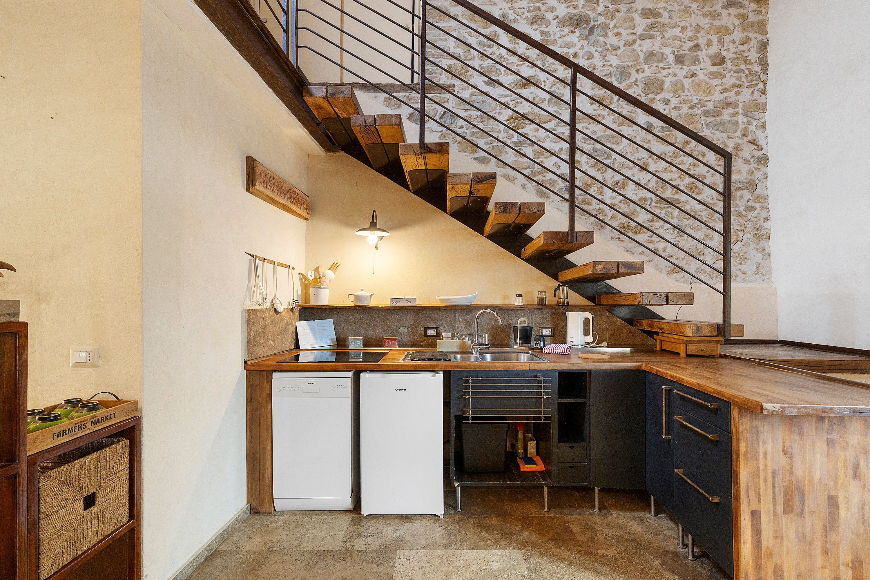 Una cocina con lavavajillas integrado, un lavabo y una escalera de madera que sube a un nivel superior.