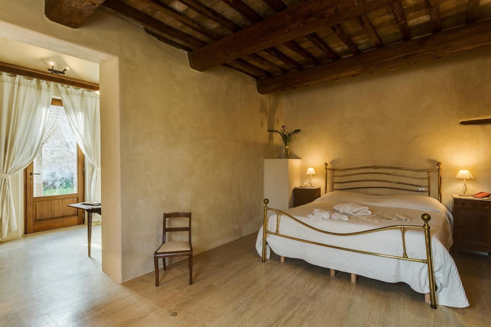 A bedroom with a bed, a chair, a nightstand, and a window with curtains.
