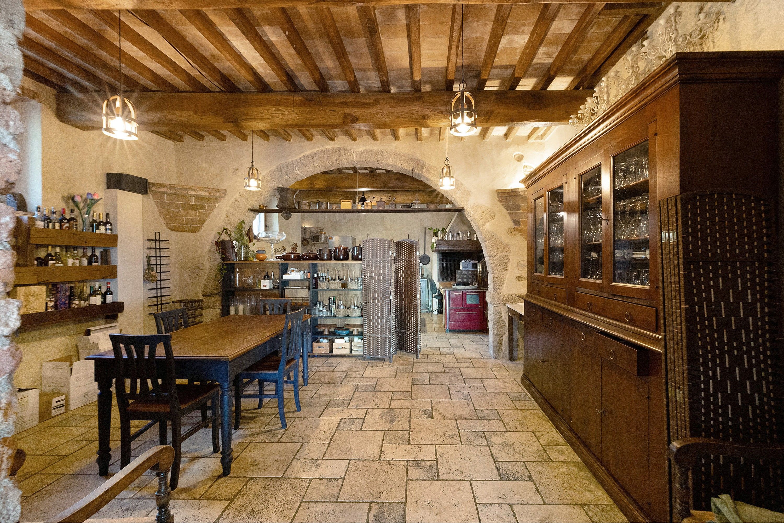 Un interno rustico con pavimento in pietra, arredi in legno e un angolo bar con bicchieri.