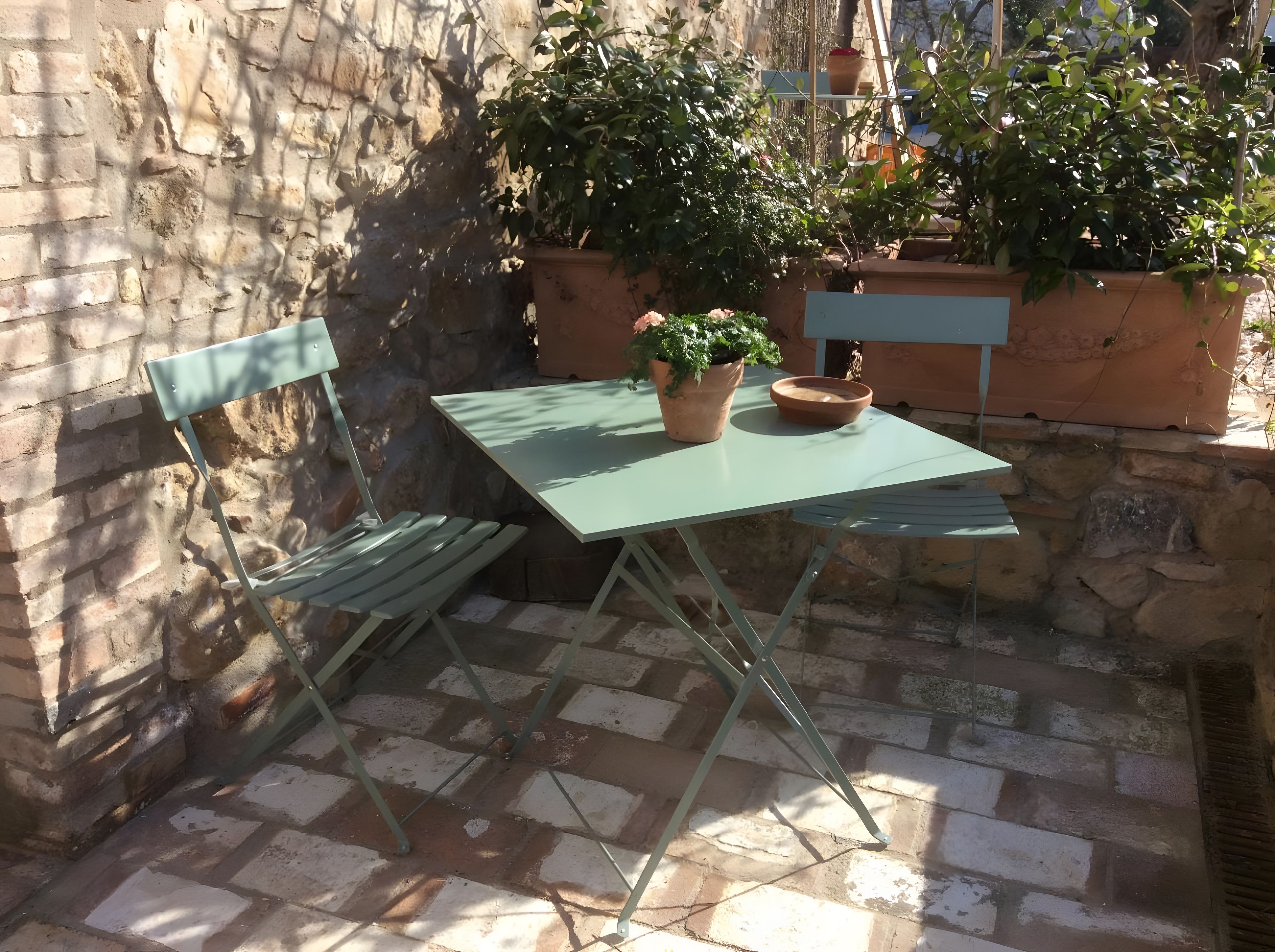 Eine Terrasse mit Tisch und Stühlen, umgeben von Steinmauern und Kübelpflanzen.