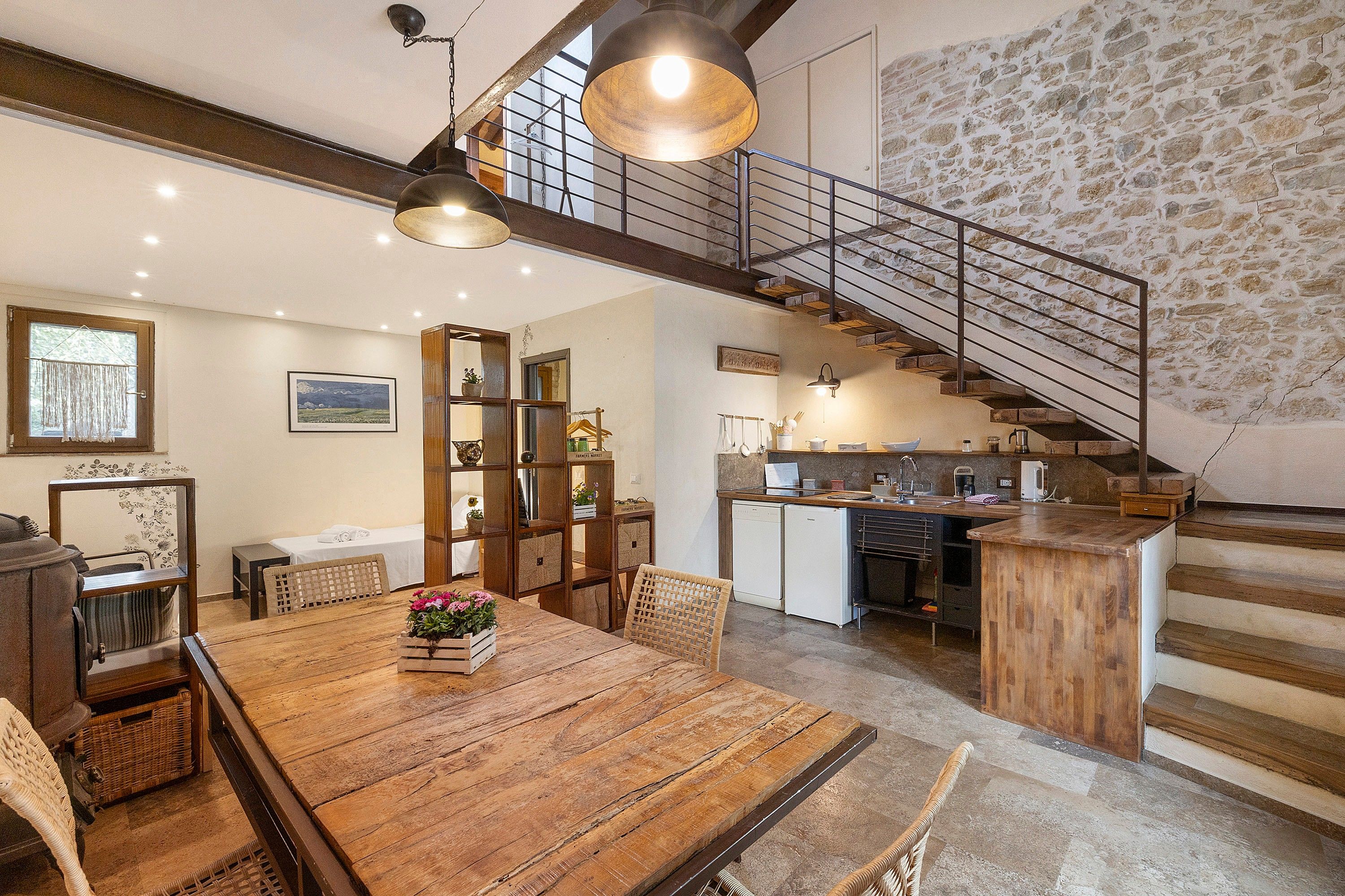 Un'ampia cucina con una parete in pietra, un tavolo da pranzo in legno con sedie e una scala che conduce a un piano superiore.