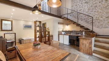 Un'ampia cucina con una parete in pietra, un tavolo da pranzo in legno con sedie e una scala che conduce a un piano superiore.