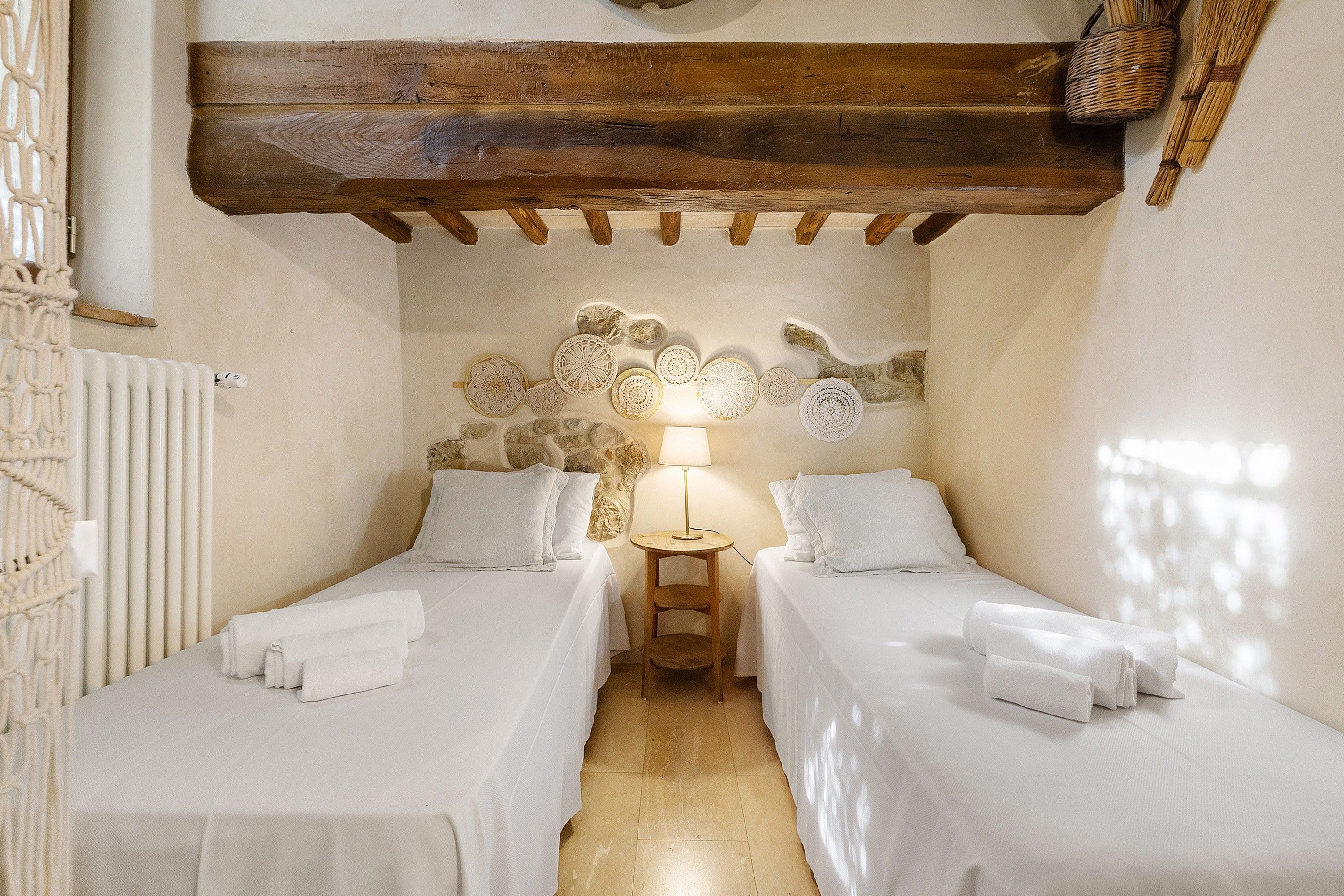 Una stanza con due letti, una parete decorata con motivi circolari, un soffitto in legno e un termosifone.