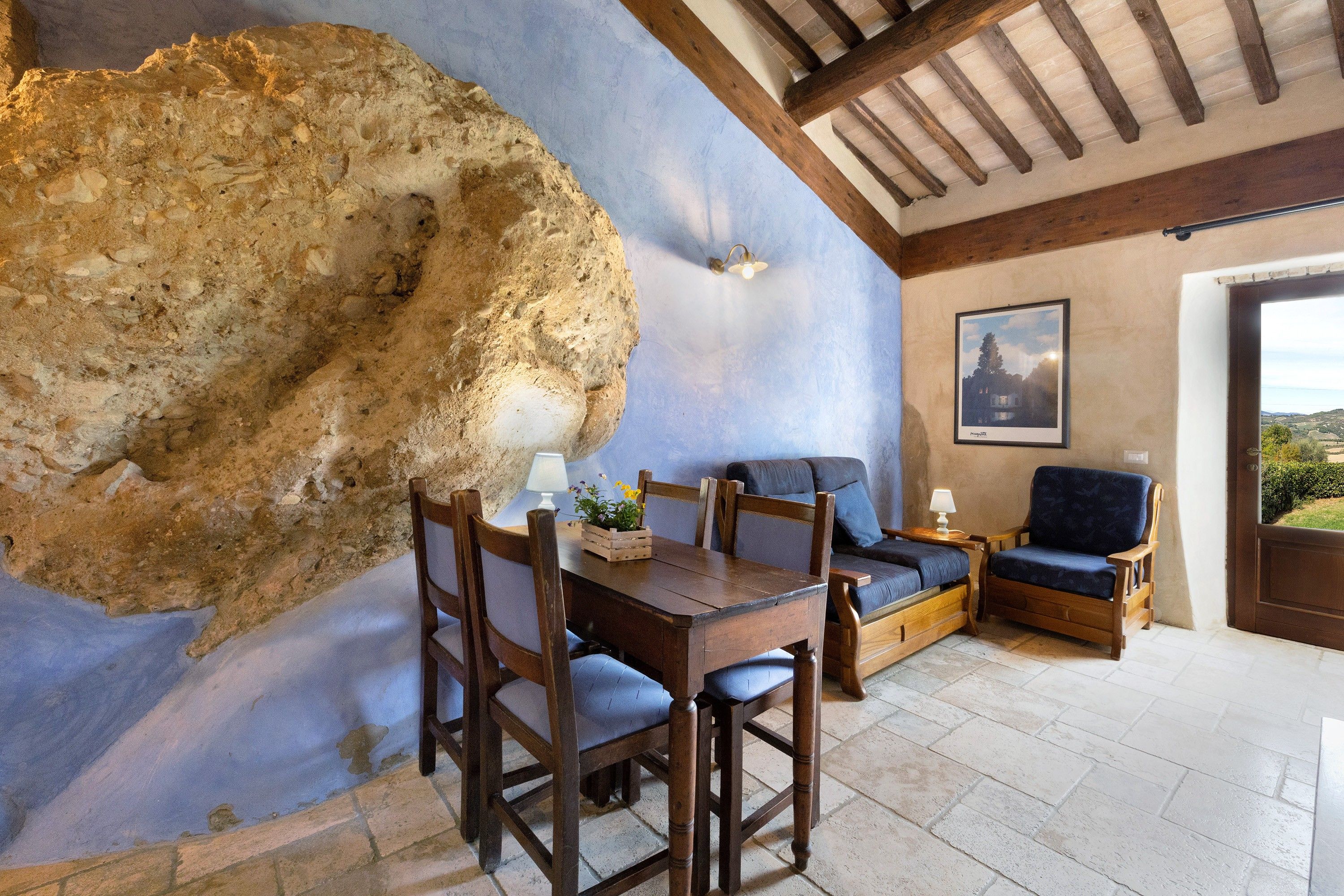 Un interior rústico con pared de piedra, muebles de madera y un cuadro en la pared.
