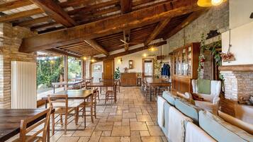 Un'ampia sala da pranzo con tavoli e sedie in legno, un camino in mattoni e vista sul verde circostante.