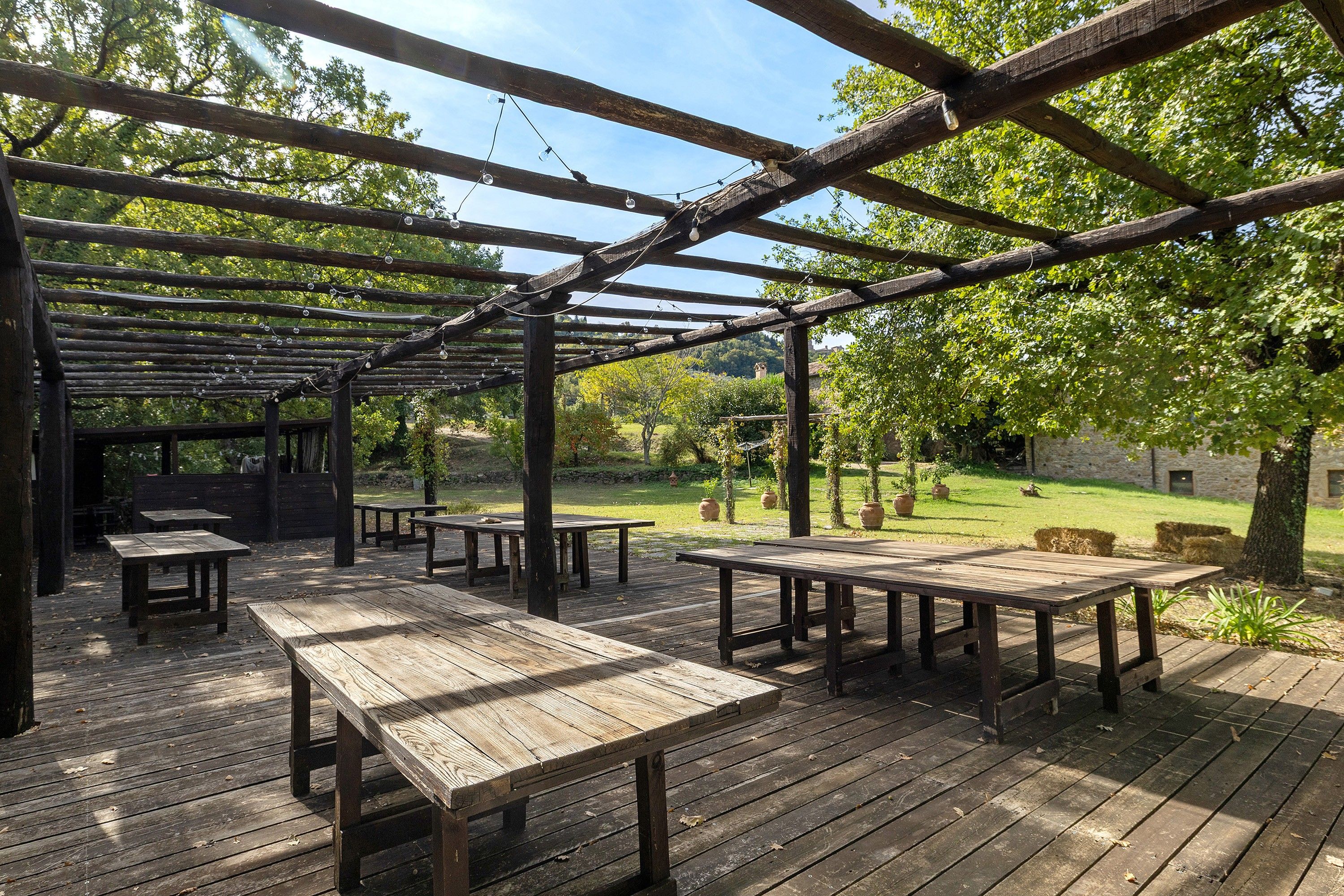 Eine Holzterrasse im Freien mit Picknicktischen und einer Pergola.