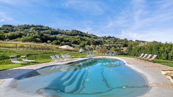 Una piscina con lettini e un pergolato, circondata da un'area verde e colline sullo sfondo.