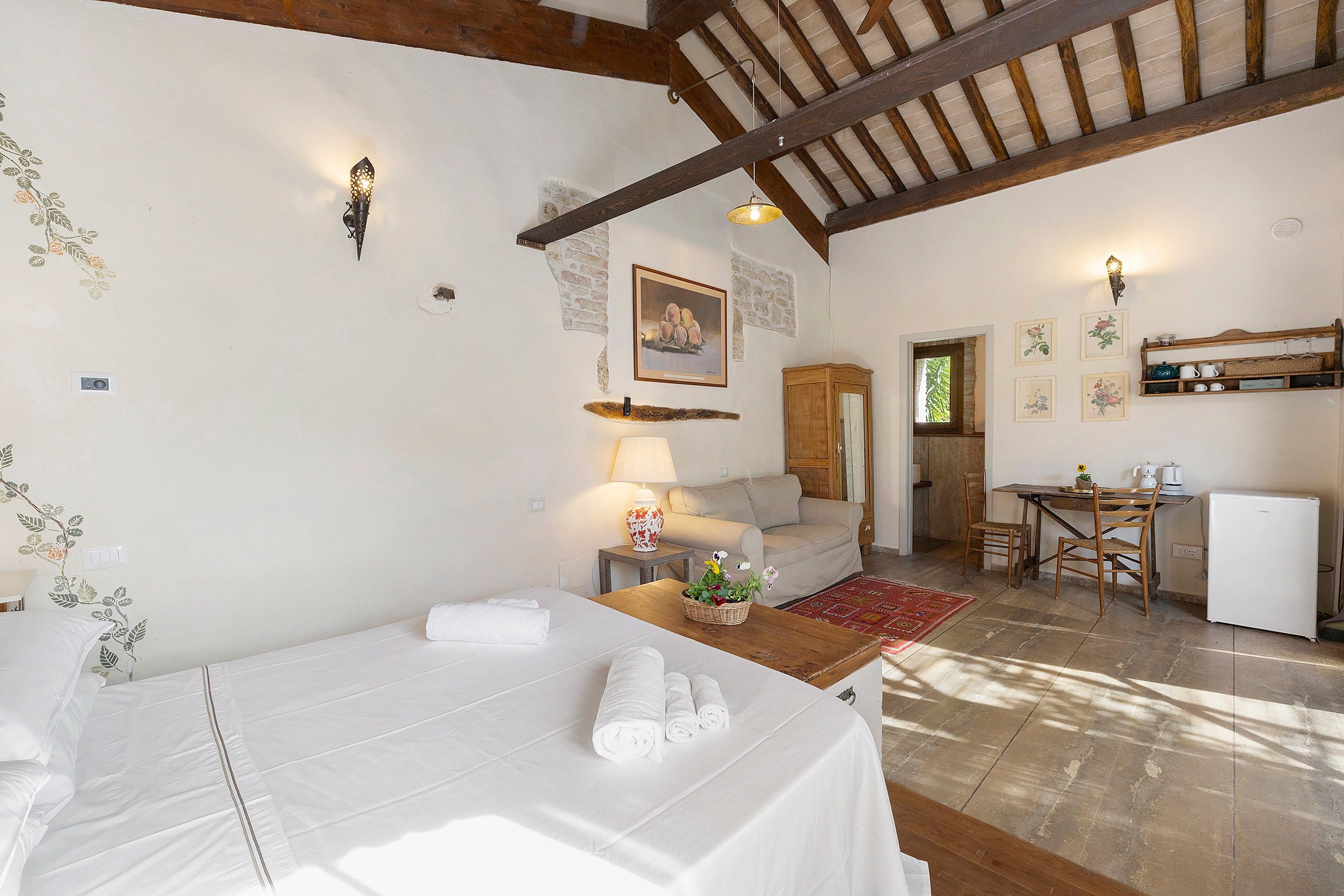 Habitación de hotel con cama, escritorio, silla, mesa, lámpara, refrigerador y ventana.