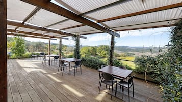 Eine Holzterrasse mit Tischen und Stühlen, eine Pergola mit einem Metalldach und Blick auf die Landschaft.