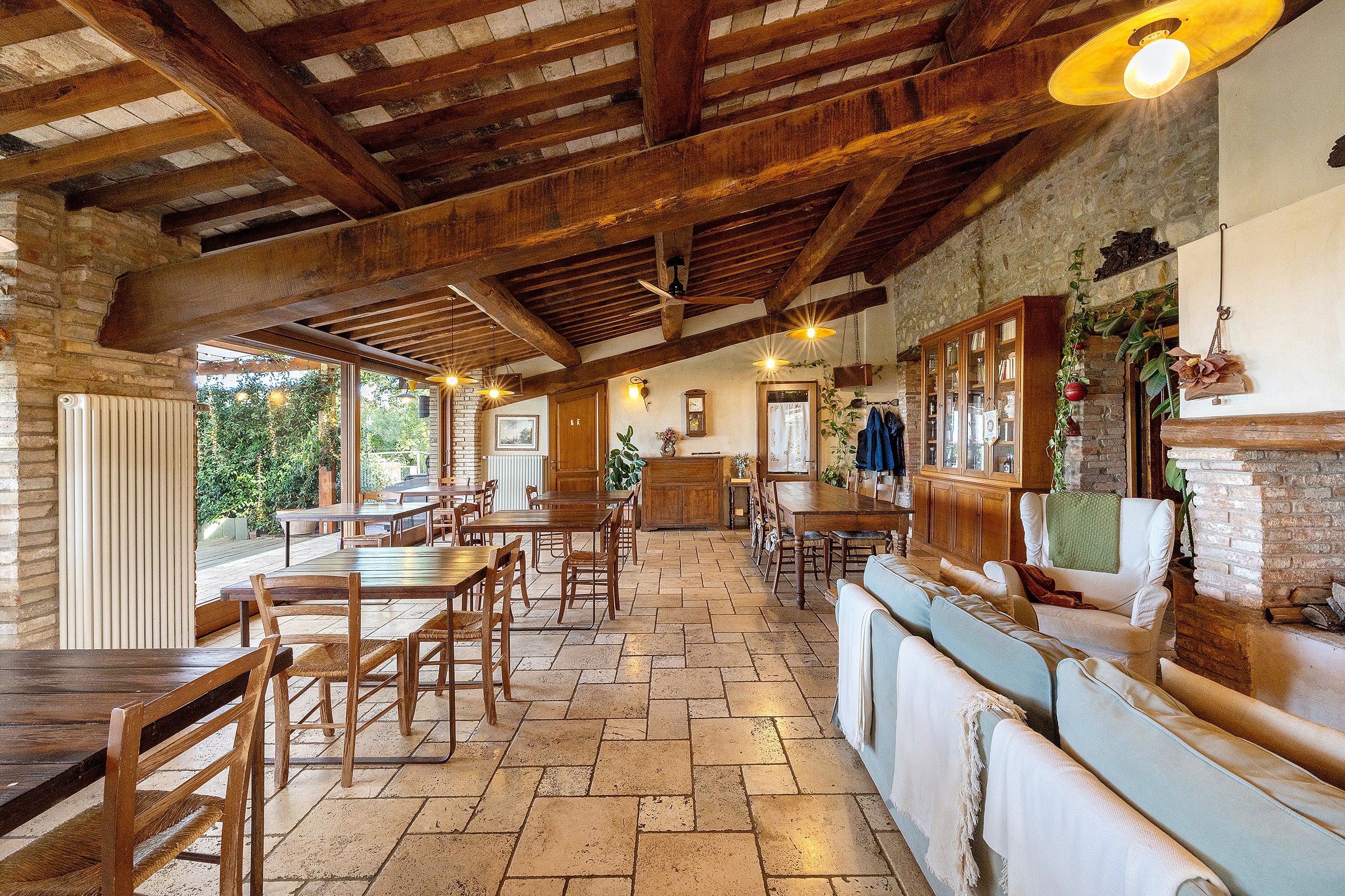 Un comedor amplio con mesas y sillas de madera, una chimenea de ladrillo y vistas a zonas verdes al exterior.