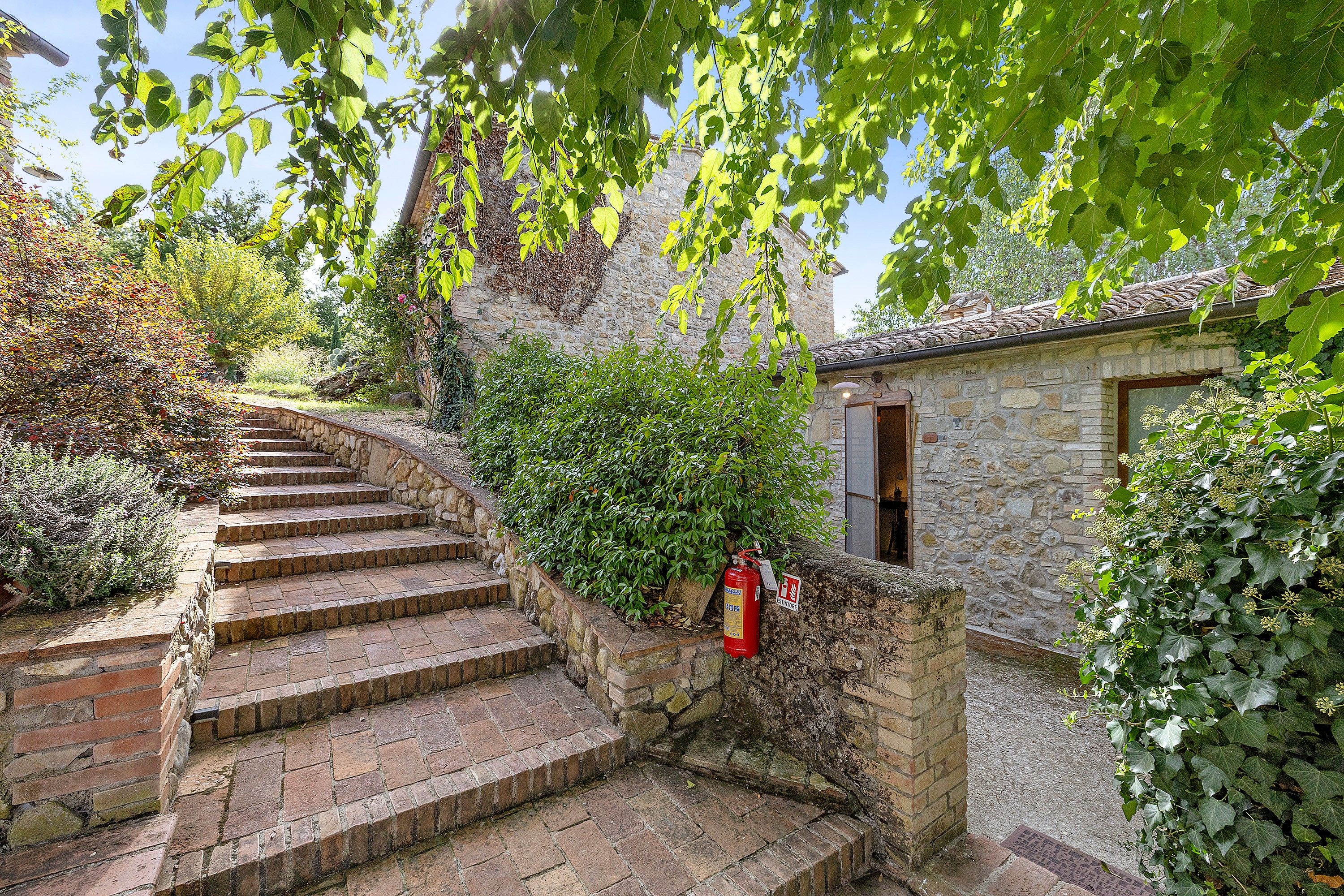 Eine steile Steintreppe führt zu einem rustikalen Steinhaus, an dessen Wand ein Feuerlöscher befestigt ist.