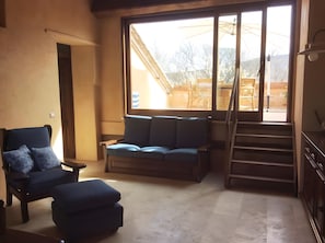 Ein Zimmer mit einem großen Fenster, einem Sofa, einem Sessel und einer Treppe.