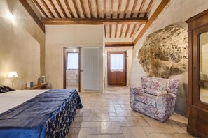 A bedroom with a bed, a chair, a radiator, and a stone wall. - Apartment 'Soffitte - Agriturismo Le Canterie' with Shared Pool, Private Terrace and Wi-Fi (Radicondoli)