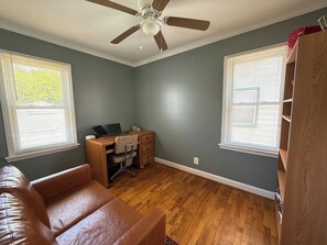 Ein Zimmer mit Deckenventilator, Schreibtisch mit Computer, Ledersofa und Holzschrank.